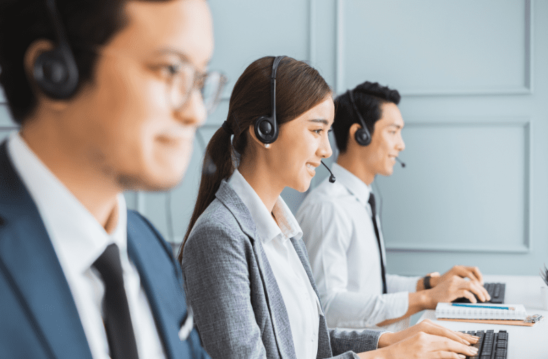 Three call center employees with headsets working at computers.