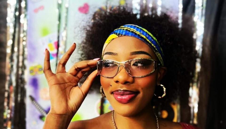 Person making an "OK" hand sign, wearing a headband, hoop earrings, and a necklace.