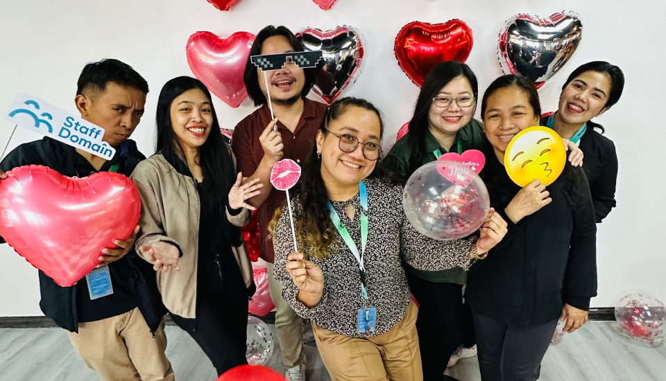 Group of people holding heart-shaped balloons and festive props.