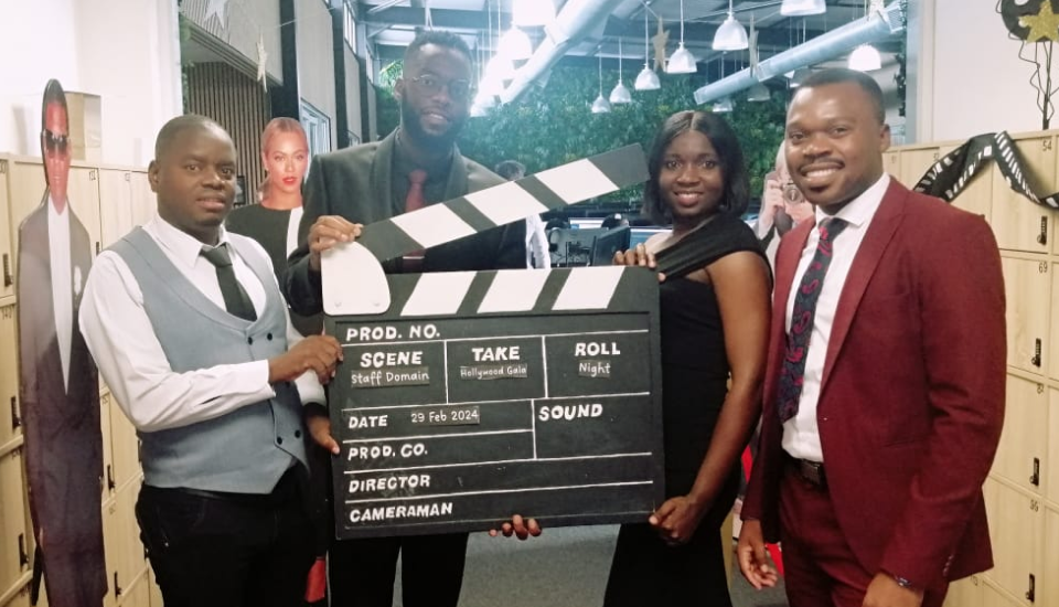 Group of people holding a clapperboard at an event, with movie decor in the background.