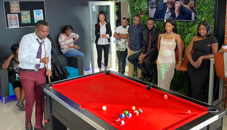 A group of people around a pool table with red felt in a modern lounge.