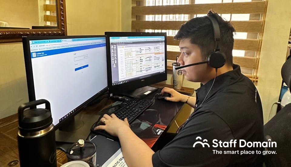 Person working on a computer with two monitors, wearing headphones, and a thermos beside them.