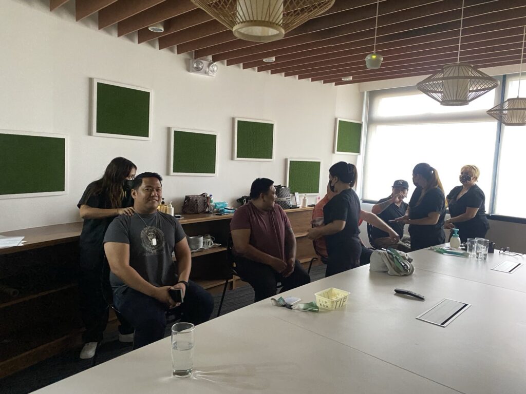 Group of people in a meeting room with green sound panels and hanging lamps.