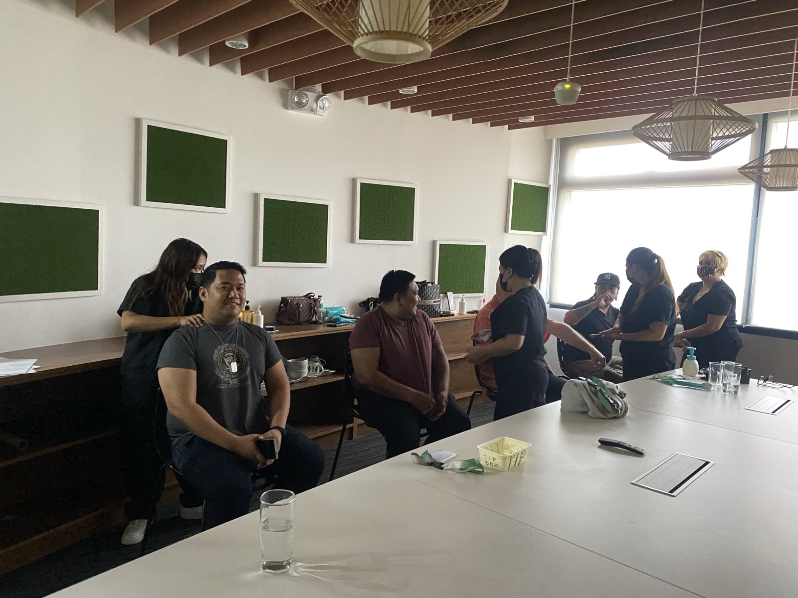 Group of people in a meeting room with green sound panels and hanging lamps.