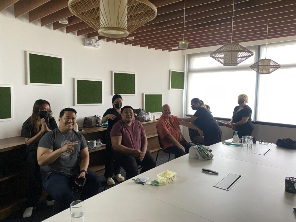 Group of people in a meeting room with green sound panels and hanging lamps.