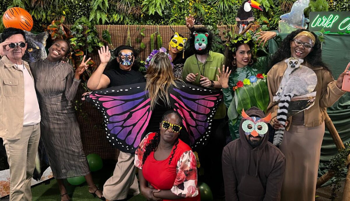 Group of people in costumes against a plant backdrop at a themed event.
