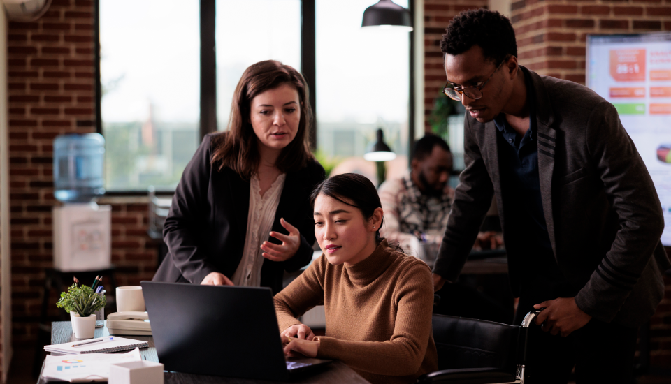Three professionals collaborating around a laptop in a modern office setting.
