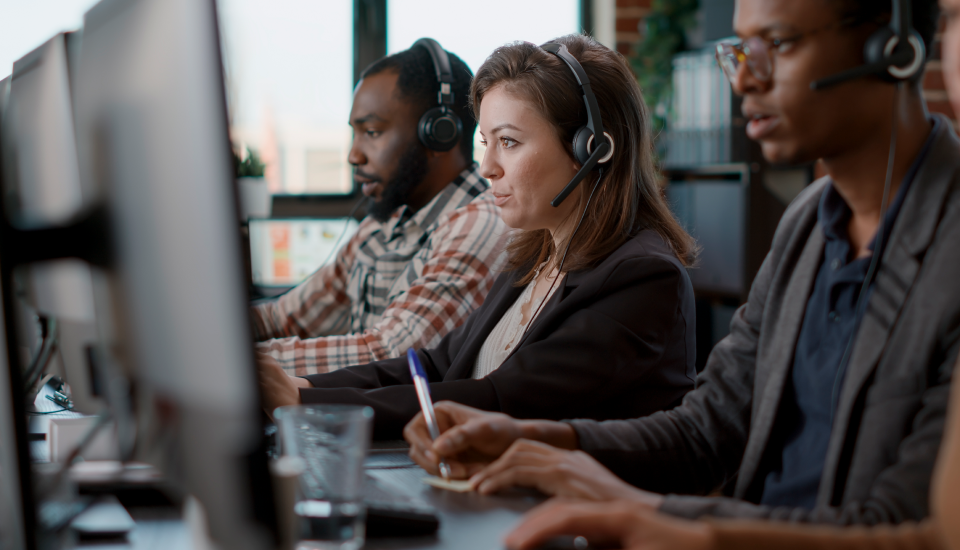 Office workers at desks with headphones and computers.