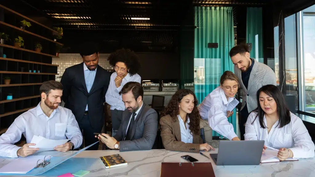 A group of professionals in a meeting room with laptops and documents on desk.