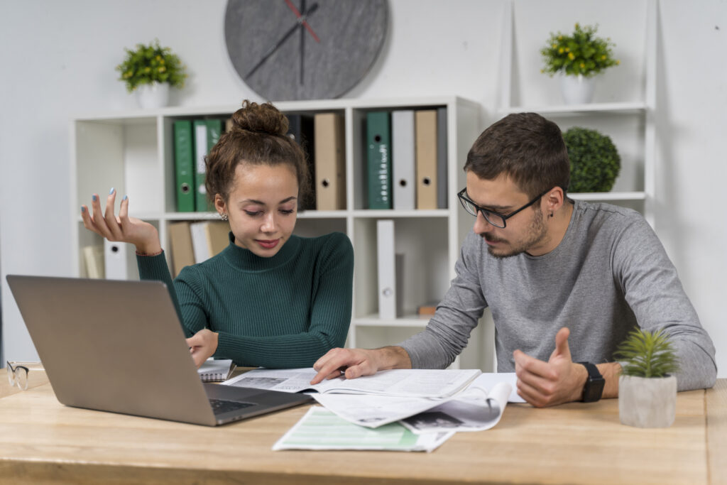 Two people with documents and laptop at a modern office desk.